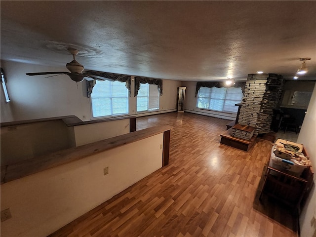 unfurnished living room featuring baseboard heating, a textured ceiling, hardwood / wood-style floors, and ceiling fan