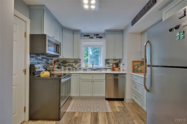 kitchen with stainless steel appliances, backsplash, light wood-type flooring, and sink