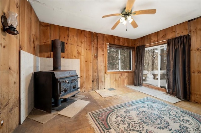 living room featuring a wood stove, wooden walls, and ceiling fan