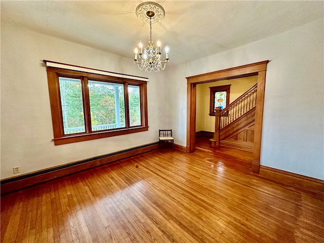 unfurnished room featuring a notable chandelier, baseboard heating, and hardwood / wood-style floors