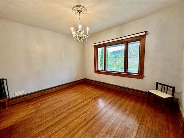 empty room featuring wood-type flooring, a chandelier, and a baseboard heating unit