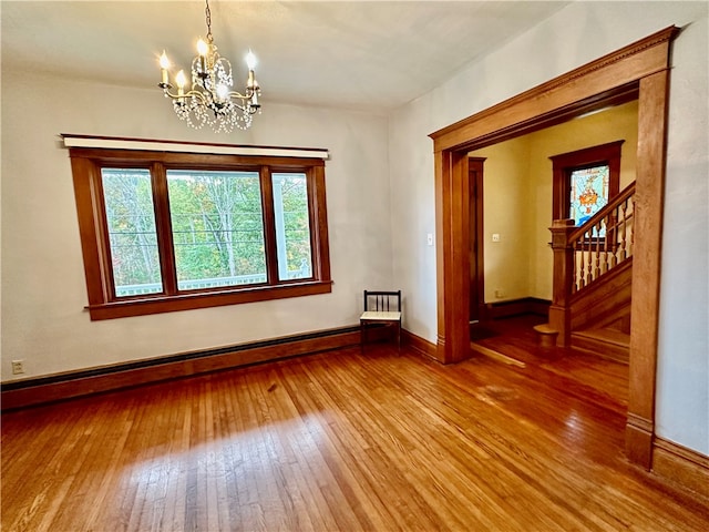 spare room featuring an inviting chandelier, hardwood / wood-style flooring, and a baseboard heating unit