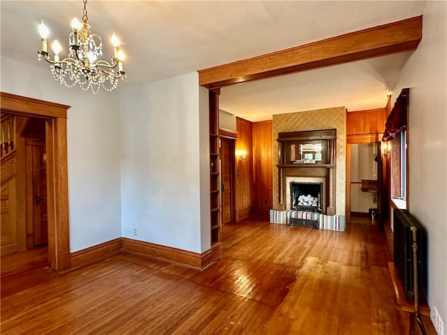 unfurnished living room featuring hardwood / wood-style flooring, a notable chandelier, beam ceiling, radiator heating unit, and a large fireplace