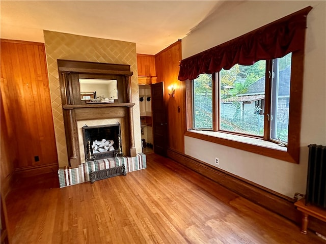 unfurnished living room with light hardwood / wood-style flooring, wooden walls, radiator, and a fireplace