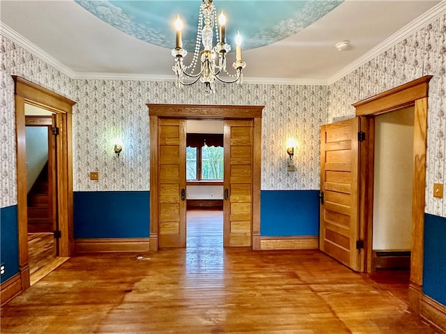 spare room featuring wood-type flooring, crown molding, and a chandelier