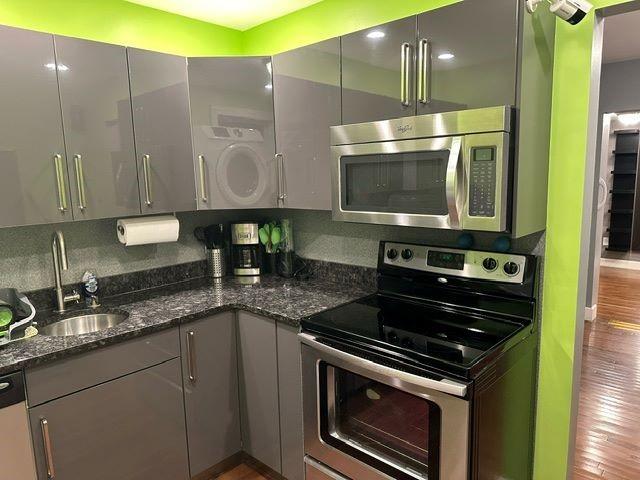 kitchen featuring dark stone counters, sink, stainless steel appliances, and wood-type flooring