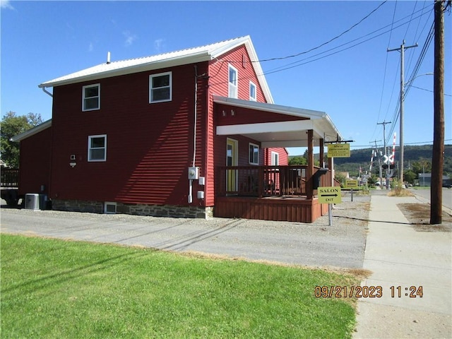 view of property exterior featuring a lawn, covered porch, and central AC