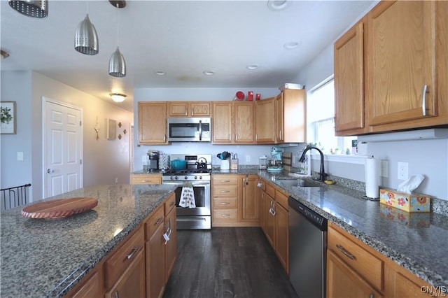 kitchen with appliances with stainless steel finishes, hanging light fixtures, dark stone countertops, dark hardwood / wood-style floors, and sink