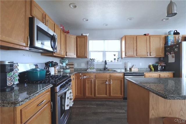 kitchen with appliances with stainless steel finishes, dark hardwood / wood-style floors, sink, and dark stone counters