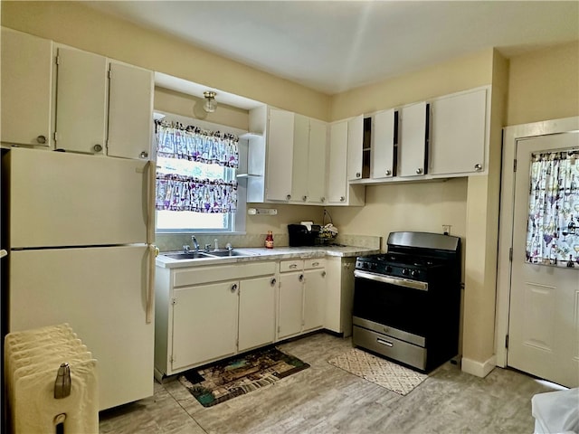 kitchen featuring white cabinetry, stainless steel gas range oven, sink, and white fridge