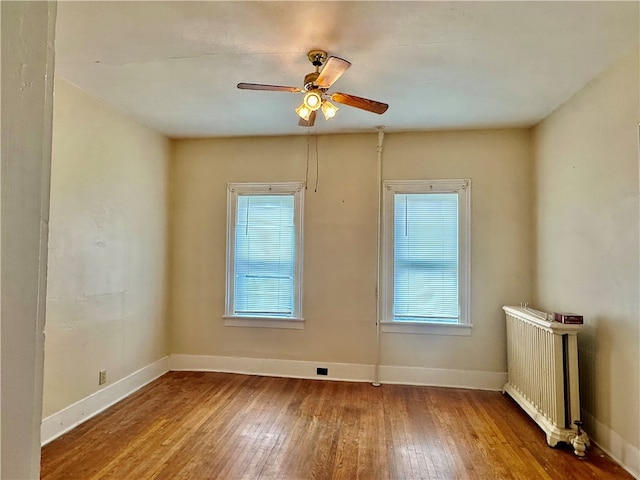 empty room featuring a wealth of natural light, ceiling fan, radiator, and hardwood / wood-style flooring