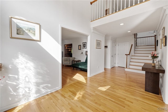 entrance foyer featuring light hardwood / wood-style flooring, a towering ceiling, and ornamental molding