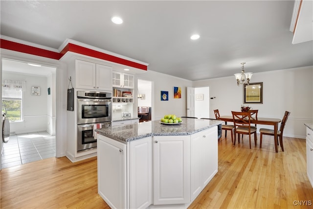 kitchen featuring light stone counters, a kitchen island, white cabinetry, double oven, and light hardwood / wood-style floors