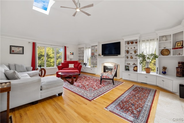 living room featuring ornamental molding, light hardwood / wood-style floors, a skylight, and ceiling fan