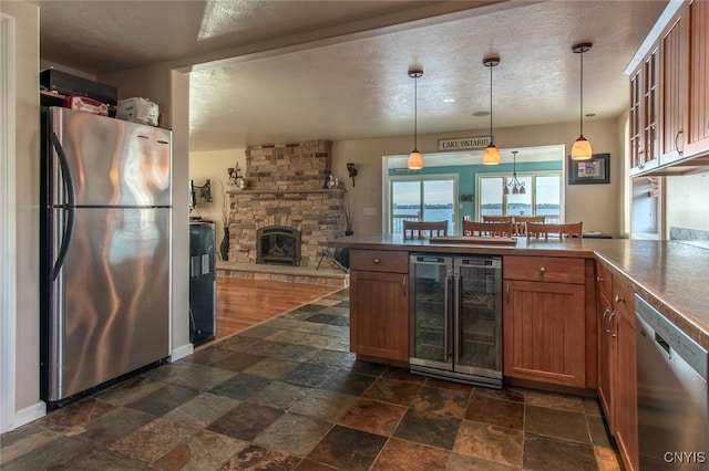 kitchen with appliances with stainless steel finishes, hanging light fixtures, a stone fireplace, and beverage cooler