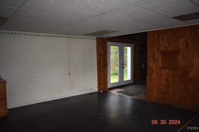 empty room with a drop ceiling, wooden walls, and baseboards