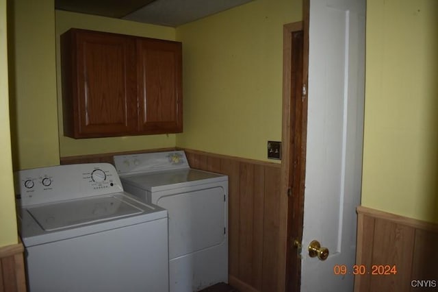 laundry room featuring a wainscoted wall, separate washer and dryer, cabinet space, and wood walls