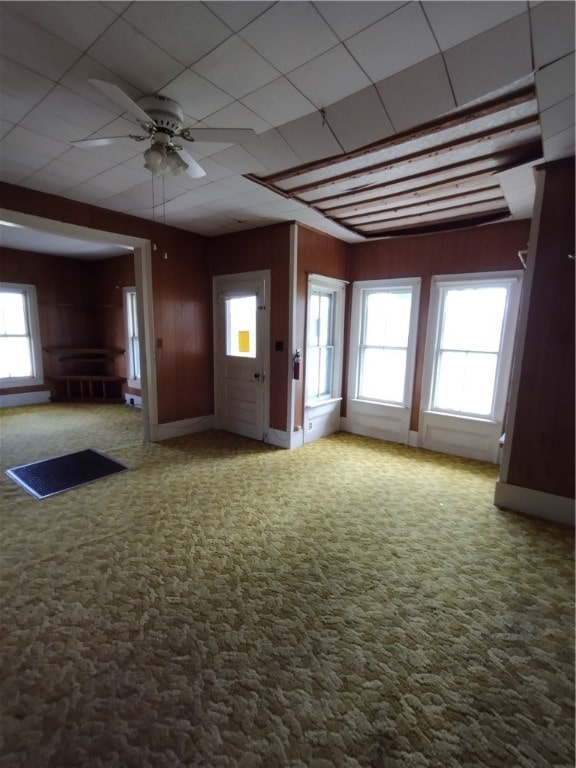 carpeted empty room featuring wooden walls and ceiling fan