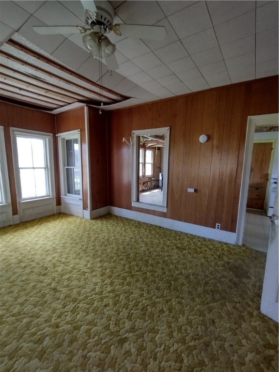 carpeted empty room featuring wood walls and ceiling fan