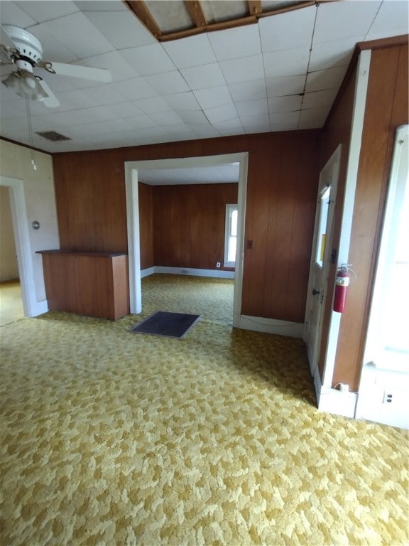 interior space with a drop ceiling, wood walls, and ceiling fan