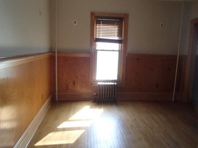 unfurnished room featuring wainscoting, radiator, wood finished floors, and wooden walls