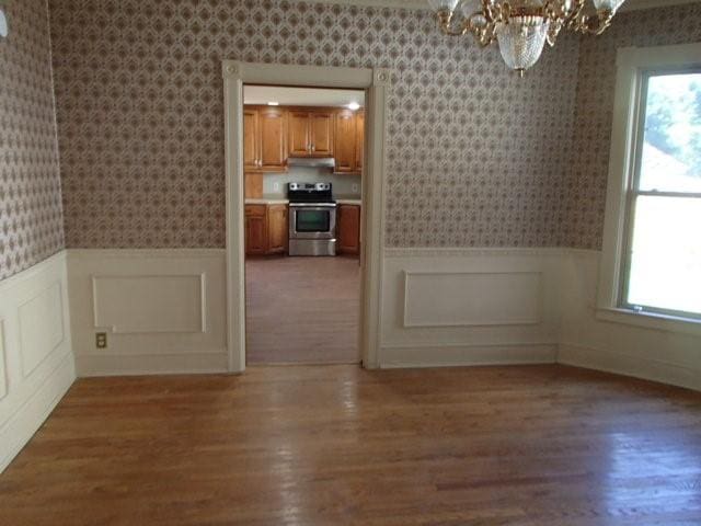 unfurnished dining area featuring an inviting chandelier, a wainscoted wall, light wood-style floors, and wallpapered walls