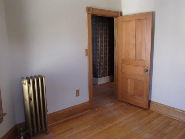 spare room featuring baseboards, radiator heating unit, and wood finished floors