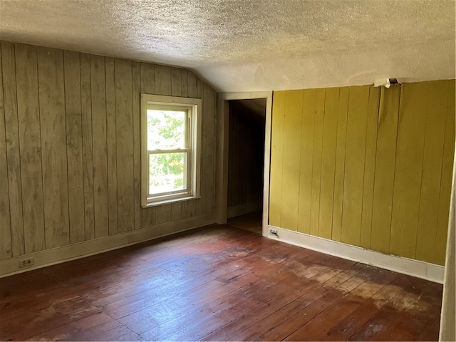 empty room with vaulted ceiling, a textured ceiling, wood walls, and dark hardwood / wood-style flooring