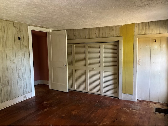 unfurnished bedroom featuring a textured ceiling, wooden walls, dark hardwood / wood-style floors, and a closet