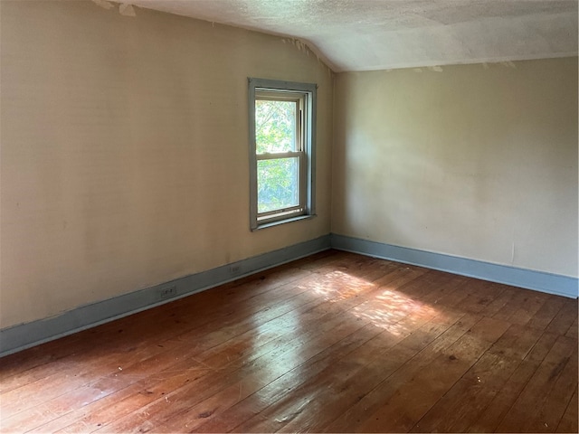 spare room featuring hardwood / wood-style flooring, lofted ceiling, and a textured ceiling