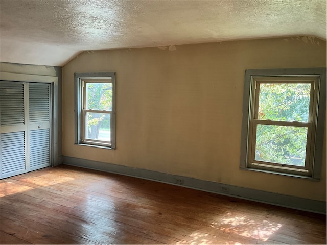 unfurnished bedroom featuring multiple windows, a textured ceiling, lofted ceiling, and light hardwood / wood-style floors