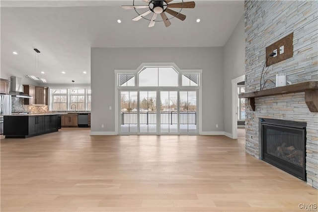 unfurnished living room with ceiling fan, sink, light hardwood / wood-style flooring, a high ceiling, and a fireplace