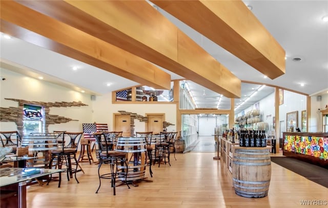 dining room with a high ceiling, beam ceiling, and light hardwood / wood-style flooring