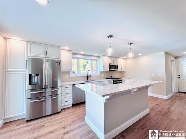 kitchen with sink, white cabinets, decorative light fixtures, appliances with stainless steel finishes, and light hardwood / wood-style floors