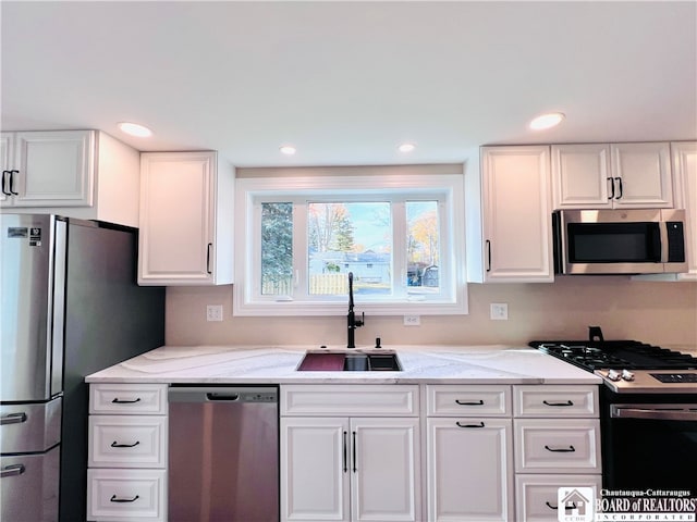 kitchen with white cabinetry, light stone countertops, appliances with stainless steel finishes, and sink