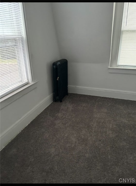 unfurnished room featuring dark carpet, vaulted ceiling, and radiator heating unit