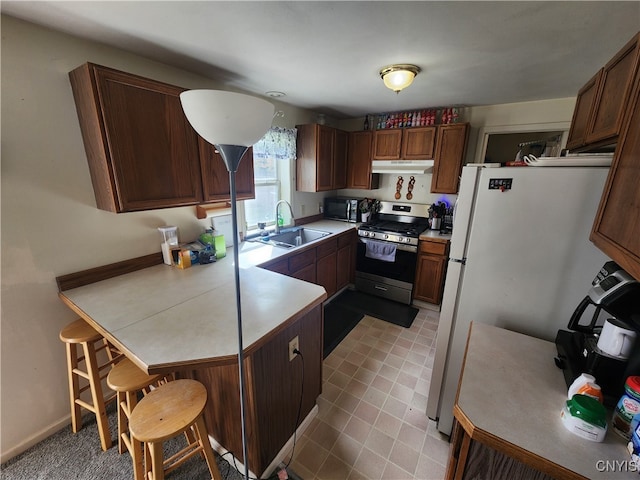 kitchen featuring a breakfast bar, white refrigerator, kitchen peninsula, stainless steel stove, and sink