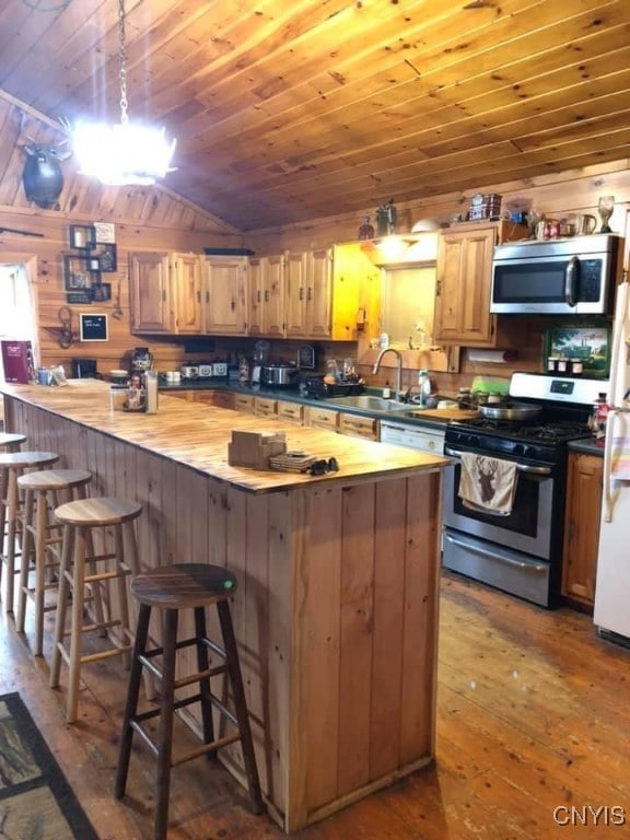 kitchen featuring sink, wooden counters, wood-type flooring, stainless steel appliances, and a kitchen bar