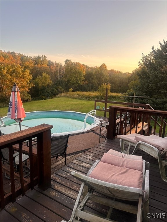 pool at dusk featuring a wooden deck and a lawn