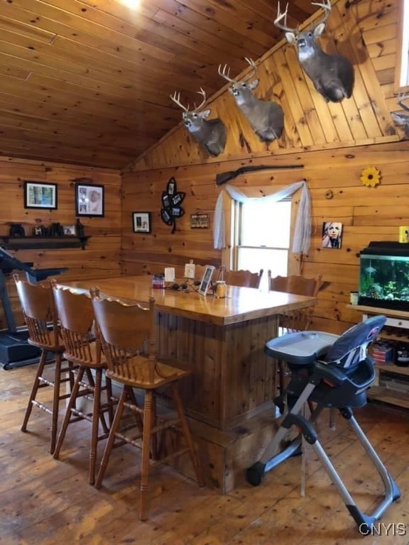 bar with wood-type flooring, wood walls, and vaulted ceiling