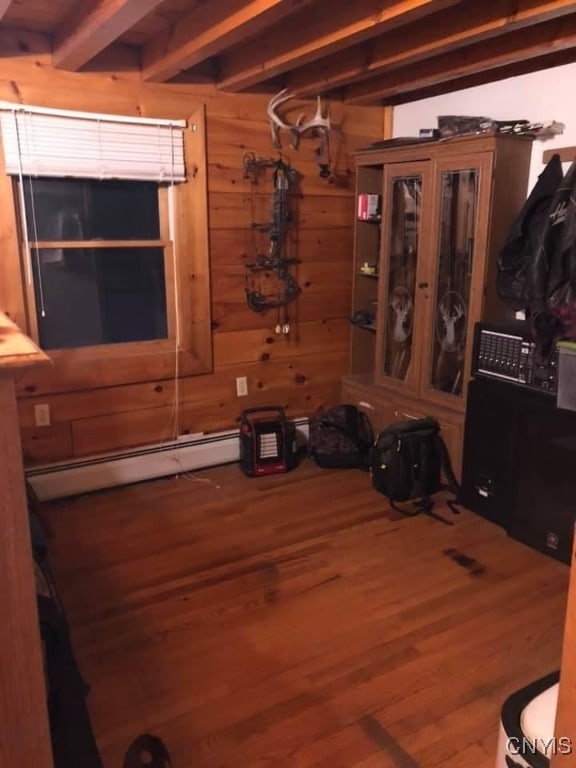 interior space with a baseboard heating unit, wood-type flooring, and wooden walls