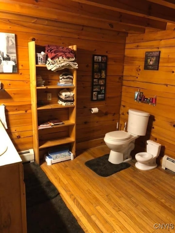 bathroom with wood-type flooring, wooden walls, baseboard heating, vanity, and toilet