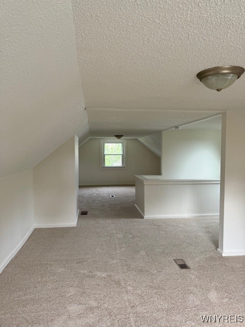 bonus room featuring lofted ceiling, a textured ceiling, and light colored carpet