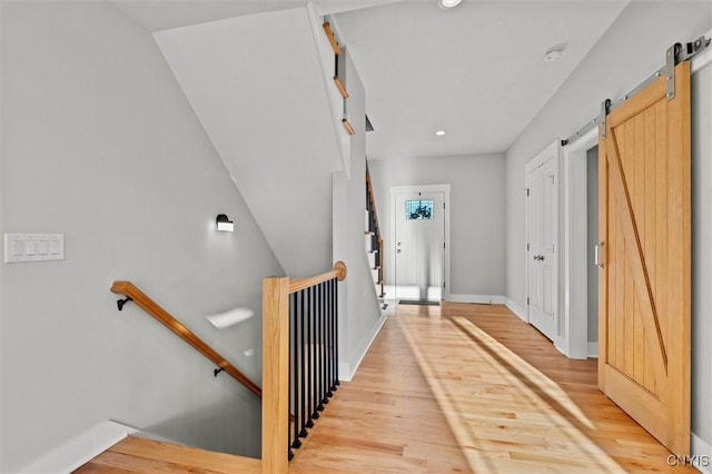 interior space with a barn door, baseboards, wood finished floors, and an upstairs landing