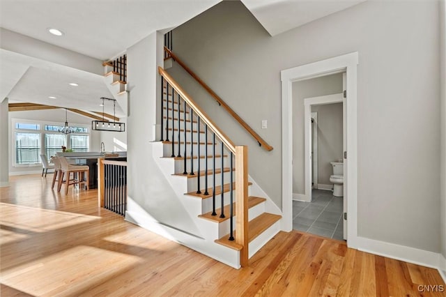 stairway with baseboards, wood finished floors, an inviting chandelier, vaulted ceiling, and recessed lighting