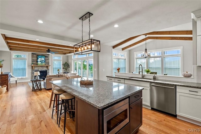 kitchen with white cabinets, appliances with stainless steel finishes, decorative light fixtures, a fireplace, and a sink