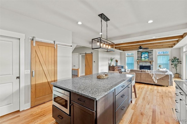 kitchen with light stone counters, pendant lighting, stainless steel microwave, a barn door, and dark brown cabinetry