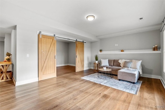 living room with visible vents, light wood-style flooring, baseboards, and a barn door