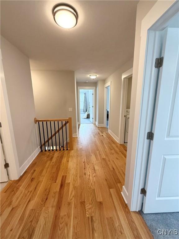 hall featuring light wood-type flooring, an upstairs landing, and baseboards