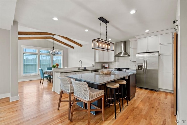 kitchen with stainless steel fridge, hanging light fixtures, wall chimney exhaust hood, and white cabinetry